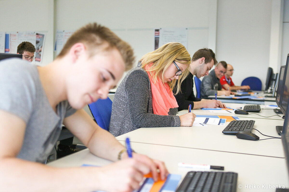 Azubis in einem Seminarraum. Azubis nehmen an einem Kurs teil und machen sich auf einem Arbeitsblatt Notizen.