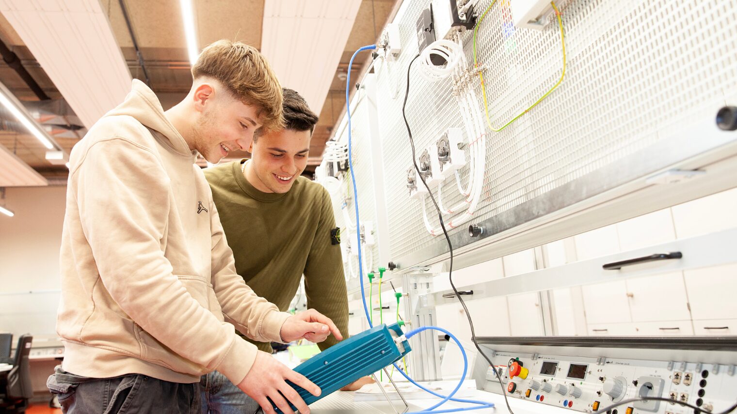 zwei junge Männer stehen in der Elektrotechnik-Werkstatt im BTZ Augsburg vor einer Schaltwand.