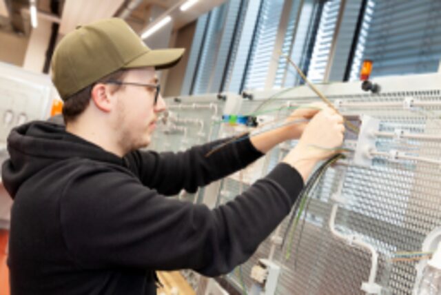 Meisterschüler steht in Elektrowerkstatt im BTZ Augsburg und arbeitet an einer Schaltwand 